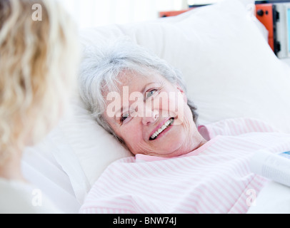 Lächelnde senior Frau liegend auf einem Krankenhausbett sprechen mit ihrer Enkelin Stockfoto