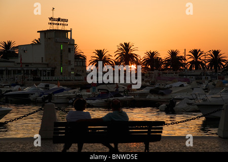 Ein paar sitzen auf einer Bank von Faro Marino und beobachten den Sonnenuntergang. Stockfoto