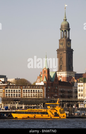 Ein Touristenboot docks im Hafen, übersehen durch das beliebte Wahrzeichen der St Michael Church in Hamburg, Deutschland. Stockfoto