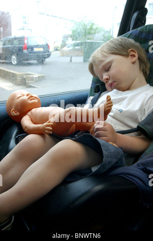 Junge schlafend im Autositz mit Puppe auf seinem Schoß. Stockfoto