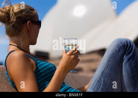 Eine Frau genießt ein Glas Wein in der Opera Bar mit der Oper im Hintergrund.  Sydney, New South Wales, Australien. Stockfoto