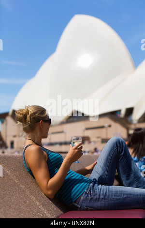 Eine Frau genießt ein Glas Wein in der Opera Bar mit der Oper im Hintergrund.  Sydney, New South Wales, Australien. Stockfoto