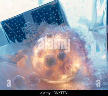 Nahaufnahme von Christbaumkugeln und Beleuchtung in Glaskugel neben verpacktes Geschenk Stockfoto