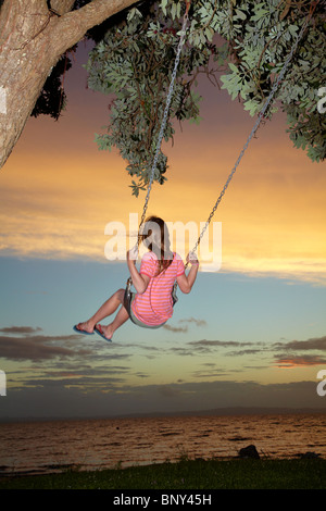 Junge Mädchen auf Seil Schaukel unter Pohutukawa Baum bei Sonnenuntergang, Themse, Coromandel, Nordinsel, Neuseeland Stockfoto