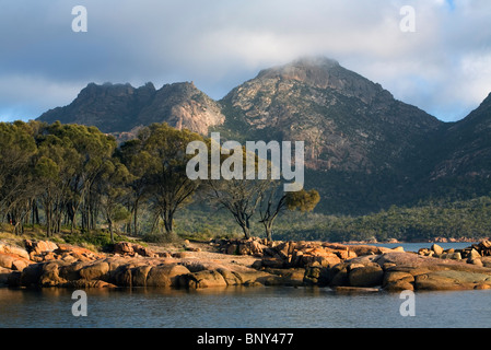 Die felsige Küste von Coles Bay mit den Gefahren Bergkette jenseits. Freycinet National Park, Tasmanien, Australien. Stockfoto