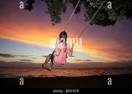 Junge Mädchen auf Seil Schaukel unter Pohutukawa Baum bei Sonnenuntergang, Themse, Coromandel, Nordinsel, Neuseeland Stockfoto