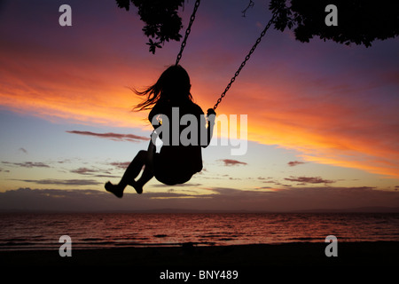 Junge Mädchen auf Seil Schaukel unter Pohutukawa Baum bei Sonnenuntergang, Themse, Coromandel, Nordinsel, Neuseeland Stockfoto