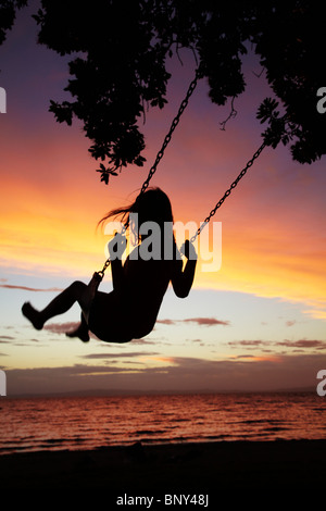 Junge Mädchen auf Seil Schaukel unter Pohutukawa Baum bei Sonnenuntergang, Themse, Coromandel, Nordinsel, Neuseeland Stockfoto