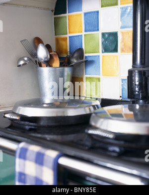Nahaufnahme von Küchenutensilien im Metalltopf auf Aga unter bunten Keramik gefliest Splash-zurück Stockfoto
