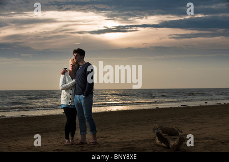 Paare, die am Strand bei Sonnenuntergang Stockfoto