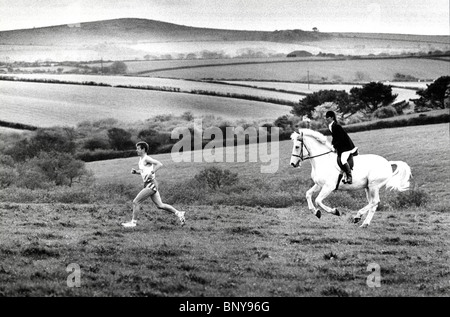 Mann läuft im Feld mit einer Frau auf Pferd nicht weit dahinter. Stockfoto