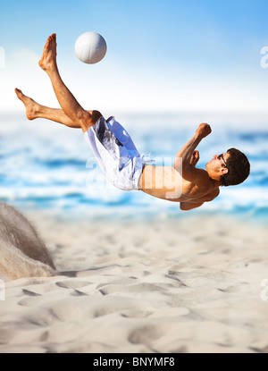 Junger Mann Fußball am Strand spielen. Stockfoto