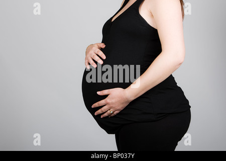 Aufnahme einer schwangeren Frau in schwarzer Kleidung vor grauem Hintergrund Stockfoto