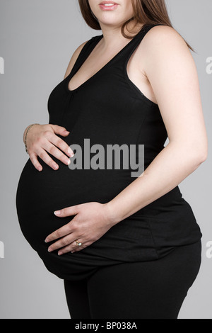 Aufnahme einer schwangeren Frau in schwarzer Kleidung vor grauem Hintergrund Stockfoto