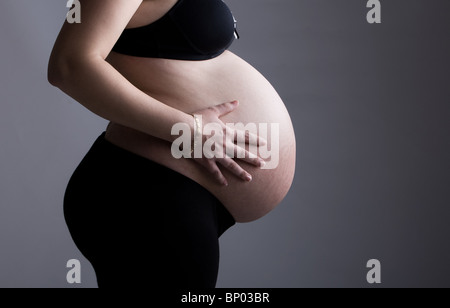 Schöne Aufnahme eine hochschwangere Frau vor grauem Hintergrund Stockfoto