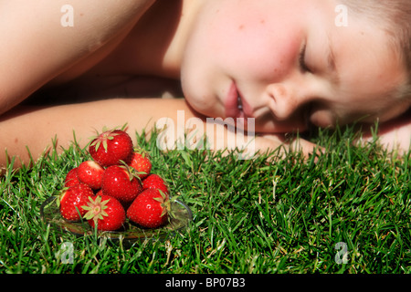 Jungen schlafen auf Rasen mit Haufen von reife Erdbeeren im Vordergrund Stockfoto