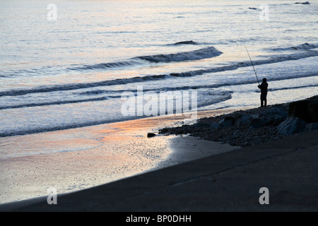 England, Dorset. Einsamer Angler Angeln in Lyme Bay vom Strand bei Charmouth. Stockfoto