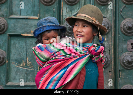 Peru, trägt ein peruanische Mädchen ihre Schwester neben die Kirchentüren der Iglesia De La Compania de Jesus in Cuscos Plaza de Armas. Stockfoto