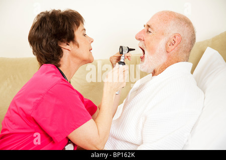 Home health care Krankenschwester verwendet einen Otoskop und Zunge Depressor, um im Mund des Patienten zu suchen. Stockfoto