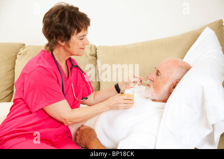 Nach Hause Krankenschwester hilft älteren Patienten ein Glas Orangensaft trinken. Stockfoto