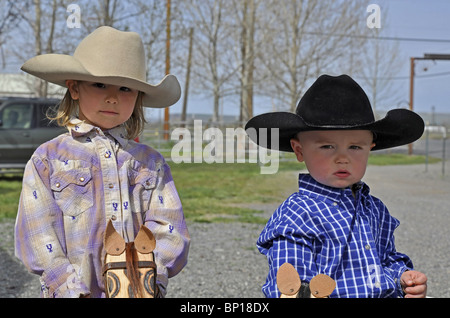 Diese niedlichen kleinen Jungen und Mädchen Geschwister sind Cowboy Hüte tragen und Holzstab Pferde tragen, wie sie einen junior Rodeo genießen. Stockfoto