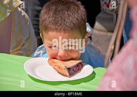 Dieser süße 4 jährige Junge hat seinen Mund auf einem Stück Blaubeerkuchen während einer Kuchenwettessen. Er ist so jung und unsicher Stockfoto