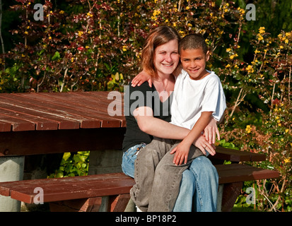 Dieses Bild ist eine glückliche Mutter und Sohn kuscheln zusammen im Freien auf einer Parkbank. Sohn ist 8 Jahre alt und Bi-Rasse sitzt auf Schoß. Stockfoto
