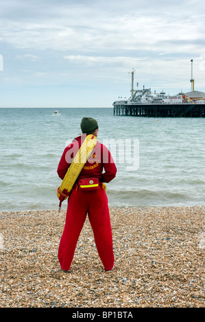 Eine männliche Strand Rettungsschwimmer im Dienst am Brighton Kiesstrand mit Brighton Pier in der Ferne in Sussex UK Stockfoto