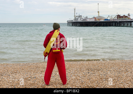 Eine männliche Strand Rettungsschwimmer im Dienst am Brighton Kiesstrand mit Brighton Pier in der Ferne Sussex UK Stockfoto