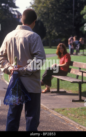 Mann, einen Blumenstrauß, einer Frau sitzt auf einer Parkbank geben Stockfoto