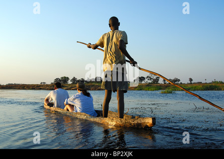 Poler mit Touristen in einem traditionellen Mokoro verfasse auf Exkursion in das Okavango Delta, Botswana Stockfoto