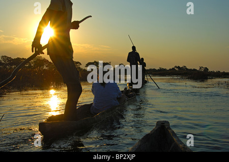 Schiffer mit Touristen im Mokoro Einbäume auf einen Sonnenuntergang Ausflug in das Okavango Delta, Botswana Stockfoto