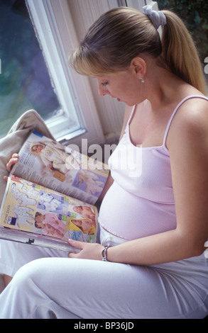 hochschwangere Frau entspannen und lesen einen Baby-Katalog Stockfoto