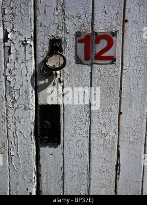Foto von Türschloss mit Peeling Seite beleuchtet Farbe. Weiße Tür mit roter Nummer 12. Stockfoto