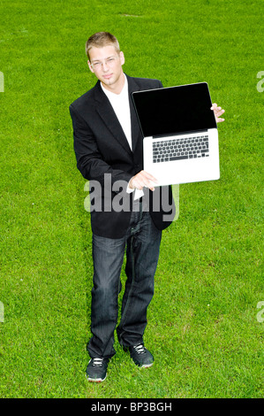 Junger Mann mit etwas auf seinem Laptop stehend auf dem grünen Rasen Stockfoto