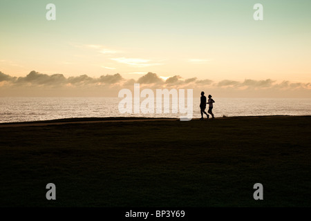 Zwei Jogger Silhouette direkt am Meer mit Sonne hinter Wolken am Horizont Stockfoto