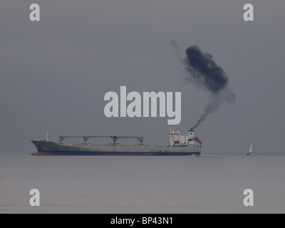 Große kommerzielle Schiff mit schwarzen Rauch aus Trichter an einem grauen Tag in der Nähe von Falmouth, Cornwall, UK Stockfoto