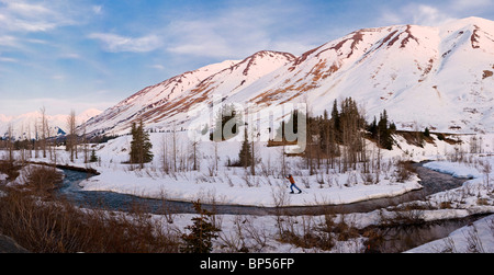 ZUSAMMENGESETZTE weibliche Langlauf in Turnagain Pass bei Sonnenaufgang mit Bertha Creek in den Vordergrund, Yunan, Alaska Stockfoto