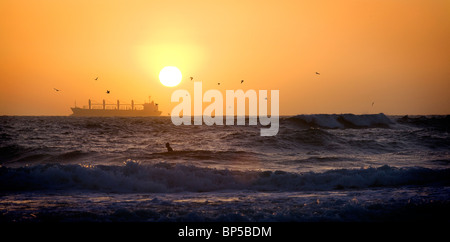 Die Silhouette eines Frachtschiffes bei Sonnenuntergang mit einem Surfer im Vordergrund abgeschossen Ocean Beach in San Francisco Stockfoto