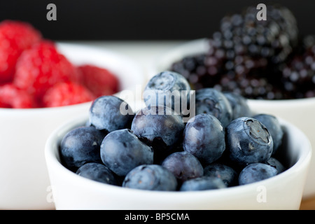 Heidelbeeren in weiße Schüssel mit Himbeeren und Brombeeren im Hintergrund. Stockfoto