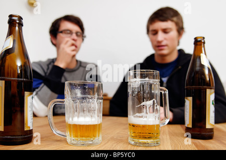 Flaschen und Gläser Bier mit zwei junge Männer im Hintergrund Stockfoto