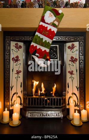 Vertikale Nahaufnahme von einem großen traditionellen Kamin mit einem prasselnden Feuer zu Weihnachten mit Strümpfen und Kerzen dekoriert. Stockfoto