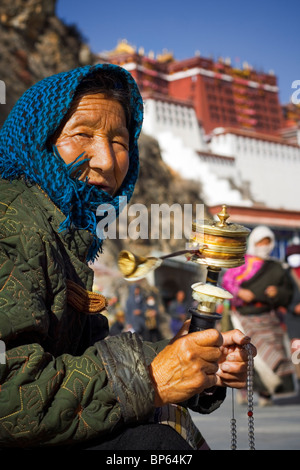 Eine ältere Frau in Tracht Kopf dreht ihr Gebetsmühle vor den Potala Palast, Lhasa, Tibet, China. 2010 Stockfoto