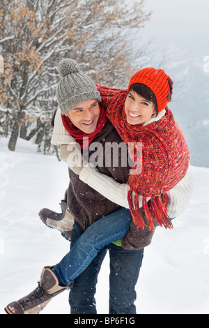 Junger Mann mit seiner Freundin Huckepack im Schnee Stockfoto