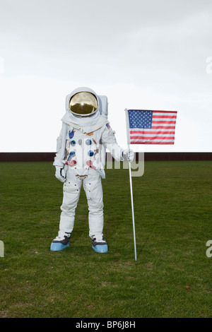 Ein Astronaut auf einer Wiese stehen, während posiert neben eine amerikanische Flagge Stockfoto