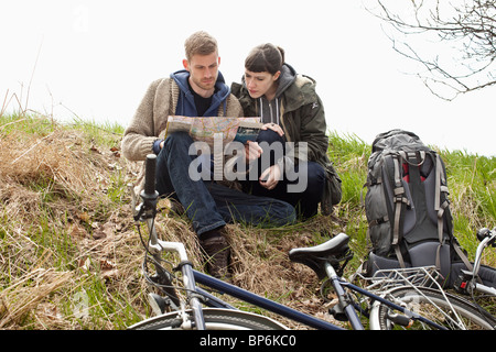 Ein paar sitzt auf einem Hügel neben ihren Fahrrädern Blick auf eine Karte Stockfoto