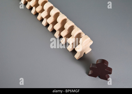 Eine braune hölzerne Strichmännchen führt eine Reihe von unbemalte Figuren aus Holz stick Stockfoto