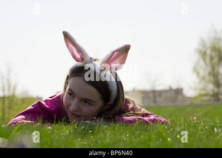 Ein Mädchen trägt Hasenohren und auf dem Rasen liegend Stockfoto