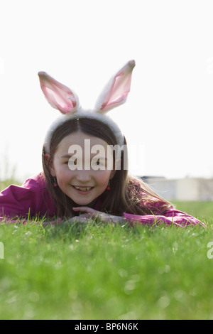 Ein Mädchen trägt Hasenohren und auf dem Rasen liegend Stockfoto