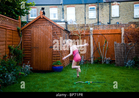 Junges Mädchen läuft durch Wasser Sprinkler in einem vorstädtischen Garten während versuchen, erfrischen Sie sich in der Hitzesommer. Foto: Jeff Gilbert Stockfoto